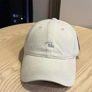 Close-up detail of beige washed cotton baseball cap with stylish black cursive letter embroidery.