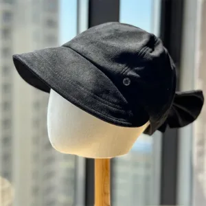 Detailed view of the black suede newsboy cap featuring a chic bow and side metallic accent.