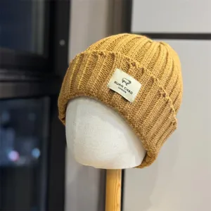 Detail shot of the mustard yellow knitted beanie with a cute sheep patch label, cozy warm.
