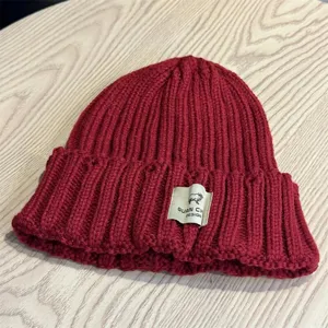 Close-up detail of cozy red knitted winter beanie hat with cute sheep patch design.