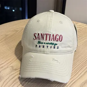 Detailed close-up of the beige distressed baseball cap featuring colorful front embroidery.