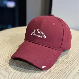 Close-up detail of a burgundy cotton baseball cap featuring white california dreaming embroidery.
