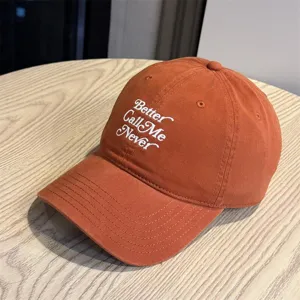 Detailaufnahme einer stylischen orangefarbenen Baseballkappe mit weißer Stickerei auf Holztisch.