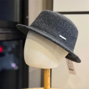 Detail view of a stylish dark grey wool bucket hat with a metal logo tag for autumn.