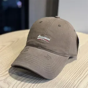 Detail view of brown washed baseball cap with white embroidery and distressed brim.