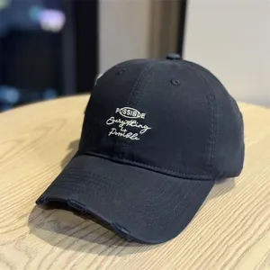 Detail close-up of the black baseball cap highlighting white text embroidery and brim.