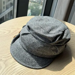 Detailed shot of grey tweed octagonal painter hat featuring side button and cozy texture.