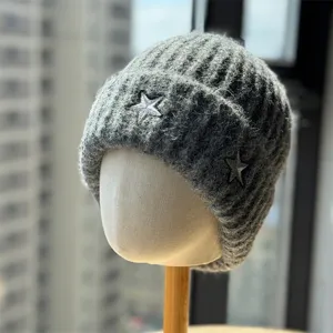 Grey knit beanie detail showing thick ribbing texture and shiny silver star embroidery patch.