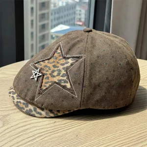 Detailed shot of brown newsboy cap featuring leopard star patch, metal pendant and brim.