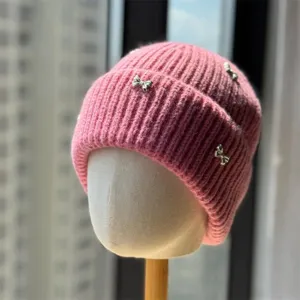 Pink knit beanie hat detail view featuring cute silver bow accents, winter warm headwear.
