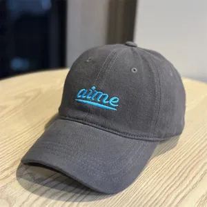 Close up detail of dark grey baseball cap featuring blue embroidered lettering and wide brim.