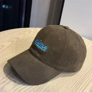 Brown corduroy baseball cap with blue embroidered letters, soft top, wide brim, casual hat.