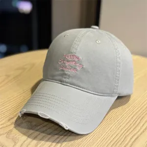 Detailed view of the grey washed baseball cap with pink embroidery and distressed brim design.