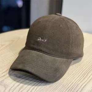Close-up detail view of the brown corduroy baseball cap with pink embroidered text front.