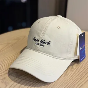 Close-up detail of beige baseball cap with black New York embroidery and side hangtag.