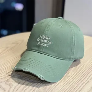 Detail view of the light green washed baseball cap featuring distressed brim and text embroidery.