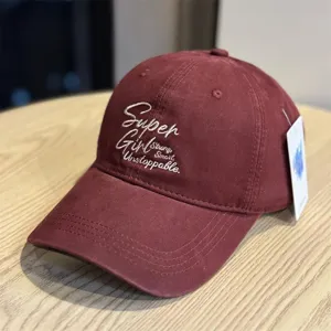 Close-up detail of the burgundy baseball cap featuring stylish white embroidered text on front.