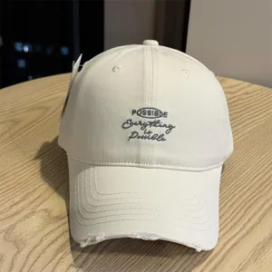 Beige cotton baseball cap featuring embroidered front text and stylish distressed brim design.