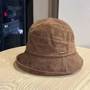 Detalle de sombrero de cubo de ante marrón con textura suave, costuras y placa de logo.