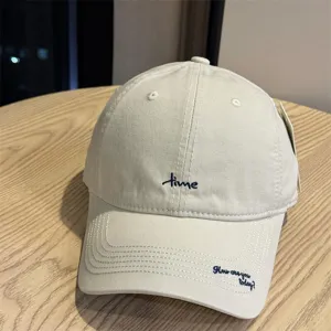 Close-up detail of beige baseball cap with stylish embroidered lettering and curved brim.