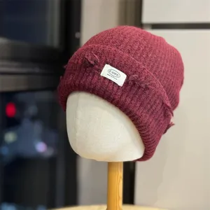 Close-up detail of the dark red knitted beanie texture and branded front cloth label.