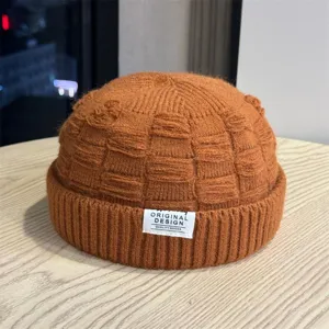 Detailopname van oranje gebreide docker muts, met getextureerd weefsel en label.