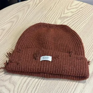 Distressed brown knit beanie detail shot, cozy winter warm hat with woven label accessory.