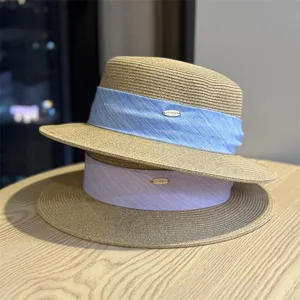 Close-up detail of stylish straw fedora hats with colorful ribbon and metal logo decoration.