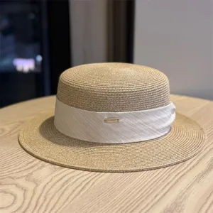 Elegant straw flat top hat with white ribbon and metal detail, perfect for summer sun protection.