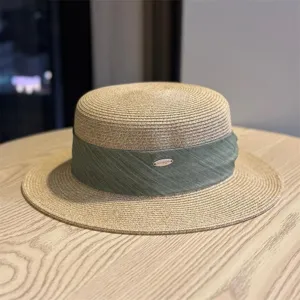 Close-up detail of the stylish straw boater hat featuring a green ribbon and metal tag.