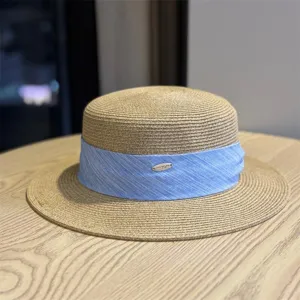 Stylish women's flat-top straw hat with light blue ribbon and metal badge detail for summer.