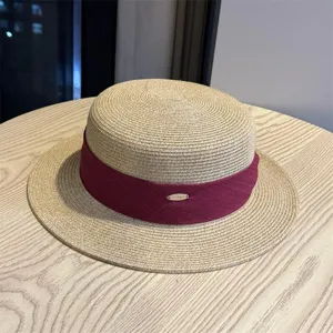 Detail view of women's flat-top straw hat with wine red ribbon and metallic accent on wood table.