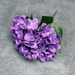 Close-up detail view of purple artificial hydrangea flower head with realistic petals and green leaves.