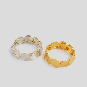 Close-up detail of the chunky metal link bracelets, featuring gold and silver geometric plates.