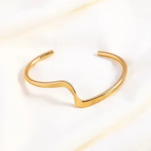 Gold open cuff bracelet, minimalist wavy geometric metal wide wristband close up detail.