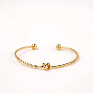 Gold open cuff bracelet detail view, minimalist metal knot design with smooth finish.