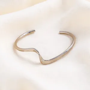 Close-up detail of minimalist wavy metal open cuff bracelet, smooth geometric design.