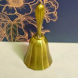 Vintage gold metal hand bell detail view, elegant embossed pattern for dining or service.