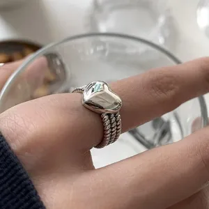 Gros plan d'une bague cœur argentée à triple anneau perlé portée au doigt, photo de détail minimaliste.