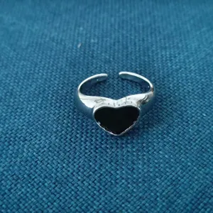 Gedetailleerde close-up van een stijlvolle open zilveren ring met een glanzend zwart hart.