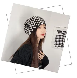 Close-up detail of stylish black and white checkered beanie hat worn by model in indoor setting.