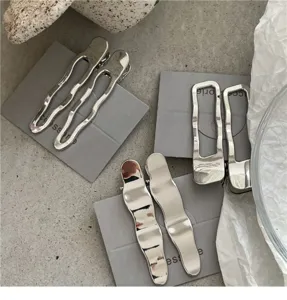 Vue de détail de pinces à cheveux en métal argenté minimaliste au design géométrique ondulé.
