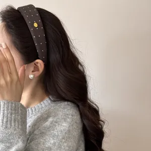 Dettaglio di un cerchietto marrone a pois indossato con orecchini di perle e maglione.