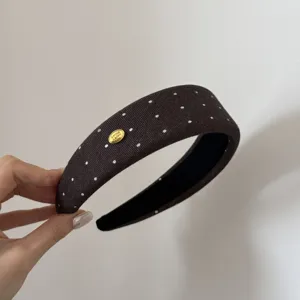 Primo piano di un cerchietto marrone a pois con un delicato dettaglio di logo in metallo.