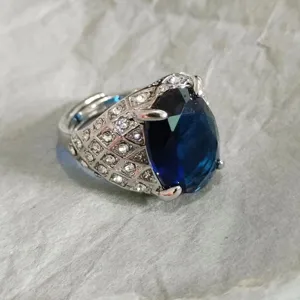 Primo piano di un anello aperto da uomo con pietra blu e dettagli in zircone su fascia.