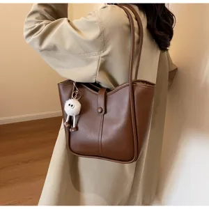 Primo piano di una borsa a tracolla in pelle marrone con ciondolo in peluche, stile quotidiano.