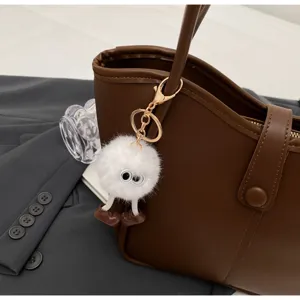 Dettaglio di un'elegante borsa tote in pelle marrone con un grazioso ciondolo di bambola di peluche.