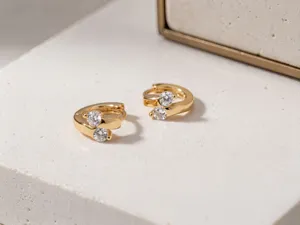 Primo piano dettagliato di orecchini a cerchio dorati con doppia pietra di zircone.