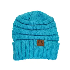 Close-up detail of the bright blue knitted beanie featuring a brown leather patch and ribbed cuff design.