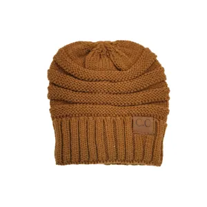 Close-up view of brown knit beanie showing textured ribbed cuff and branded leather patch.
